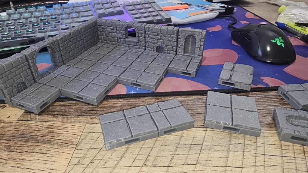 A photograph of some grey plastic 3D-printed tiles on a desk with a mouse and keyboard visible.